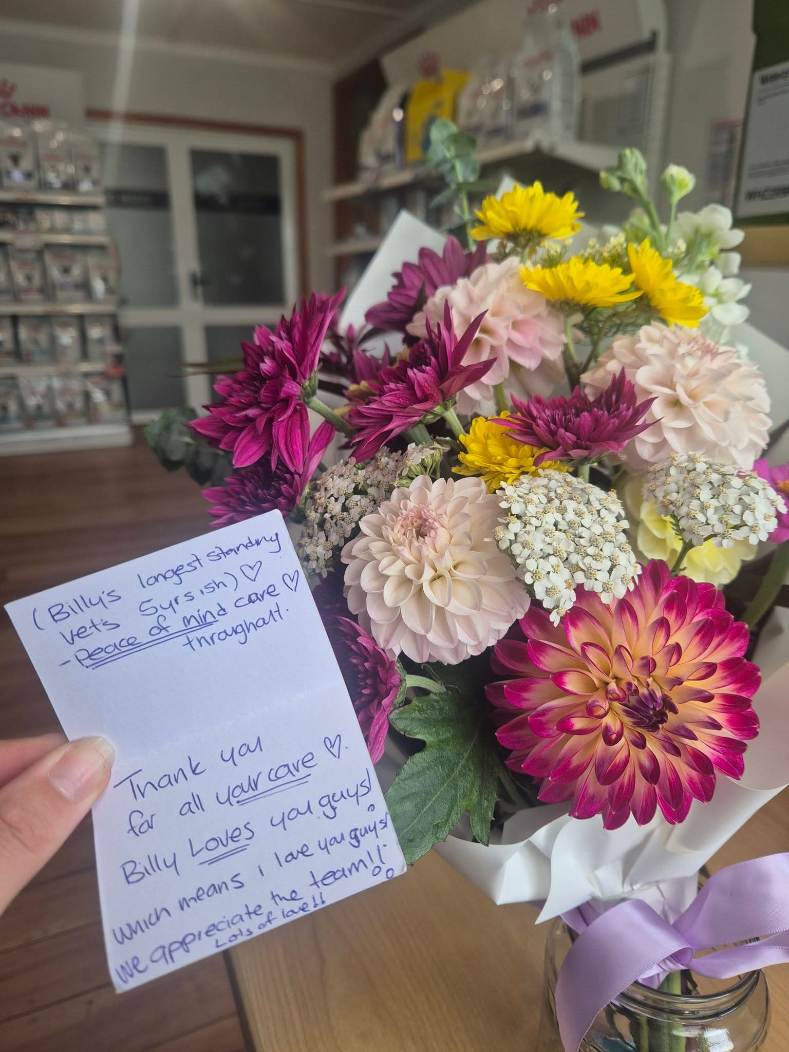 A bouquet of dahlias and a handwritten thank-you card from Billy's family, on the clinic counter